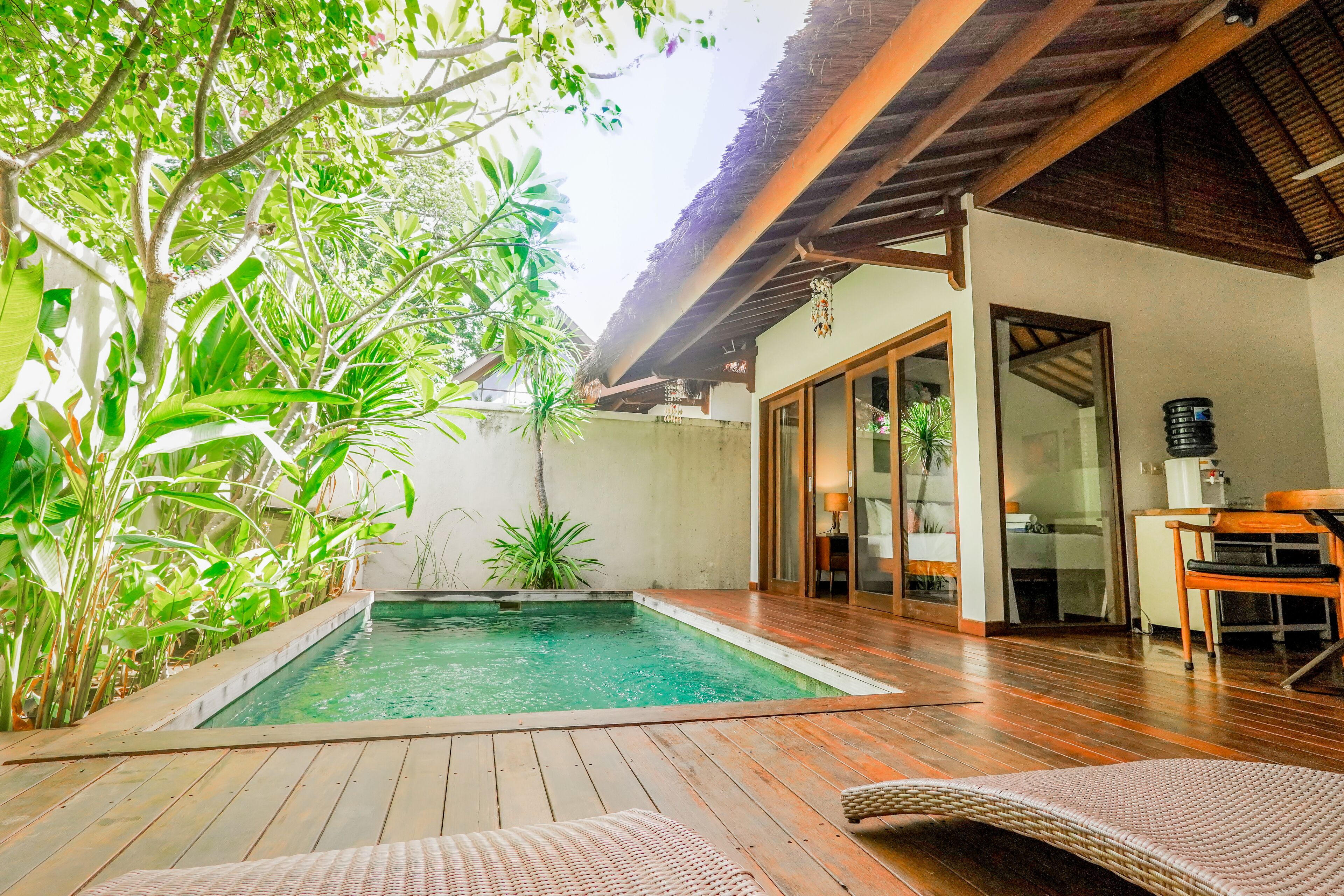 A pool area with wooden decking, a lounge chair, and a dining table.