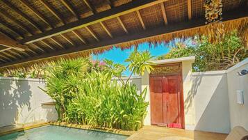 A pool area with a wooden deck, a thatched roof, and a red door.