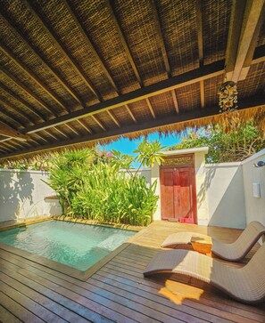 Uma área de piscina com deck de madeira, telhado de palha e uma porta vermelha.