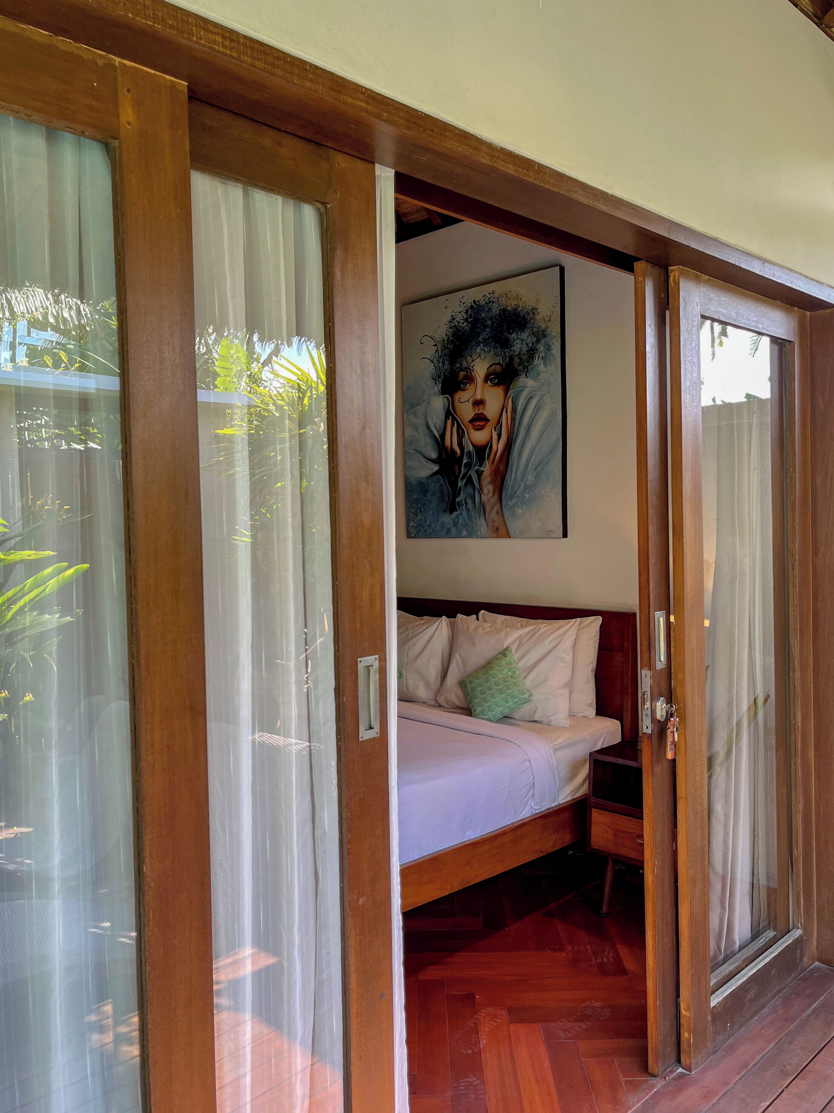 A room with a bed, wooden flooring, and a painting on the wall.