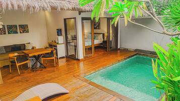 A poolside area with wooden flooring, a thatched roof, and a bed with a glass door.