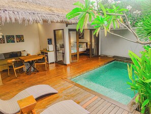 Uma área ao lado da piscina com piso de madeira, telhado de palha e uma cama com porta de vidro.