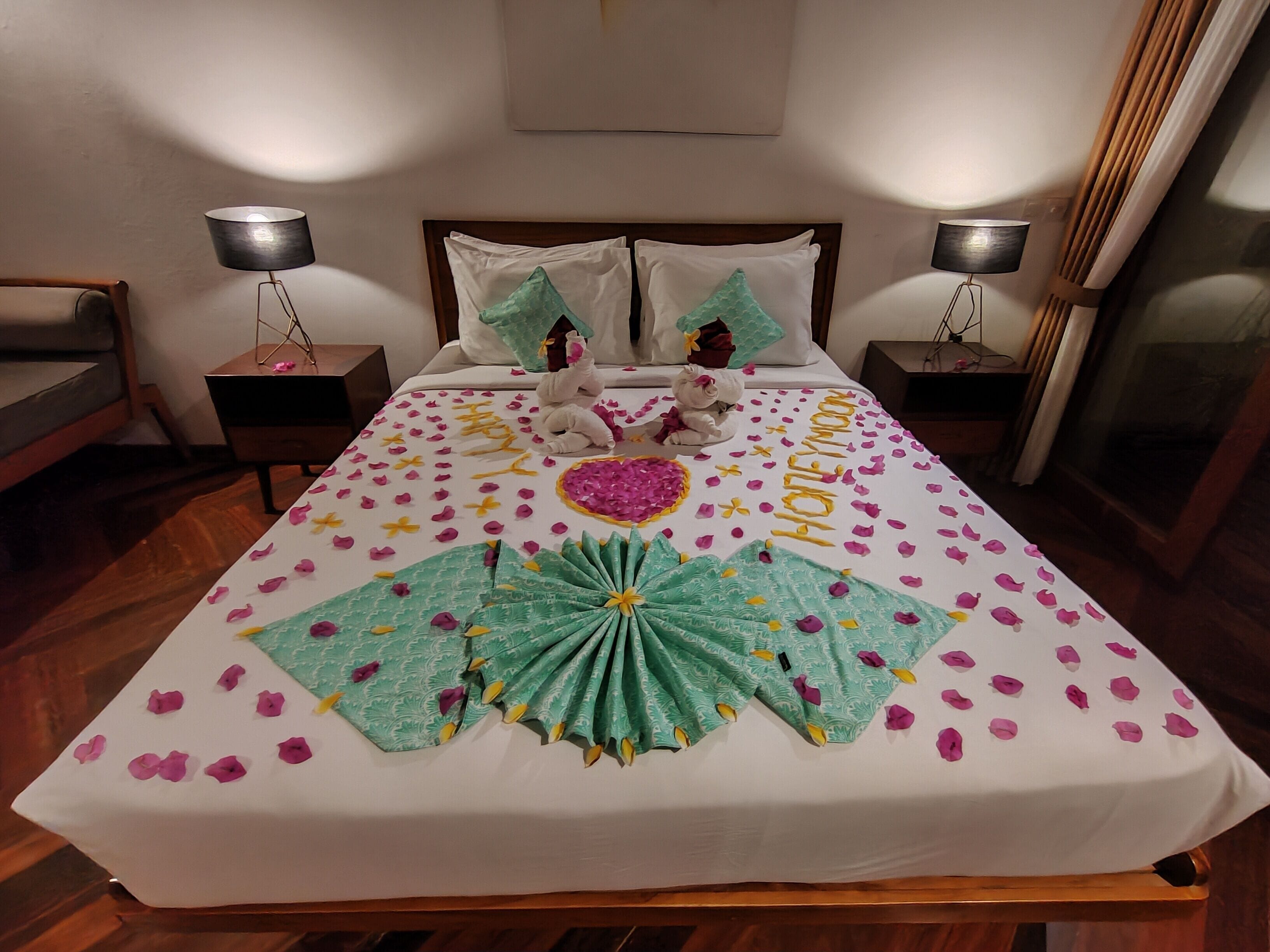 A neatly made bed with a 'honeymoon' themed bedspread, pillows, and decorative items.