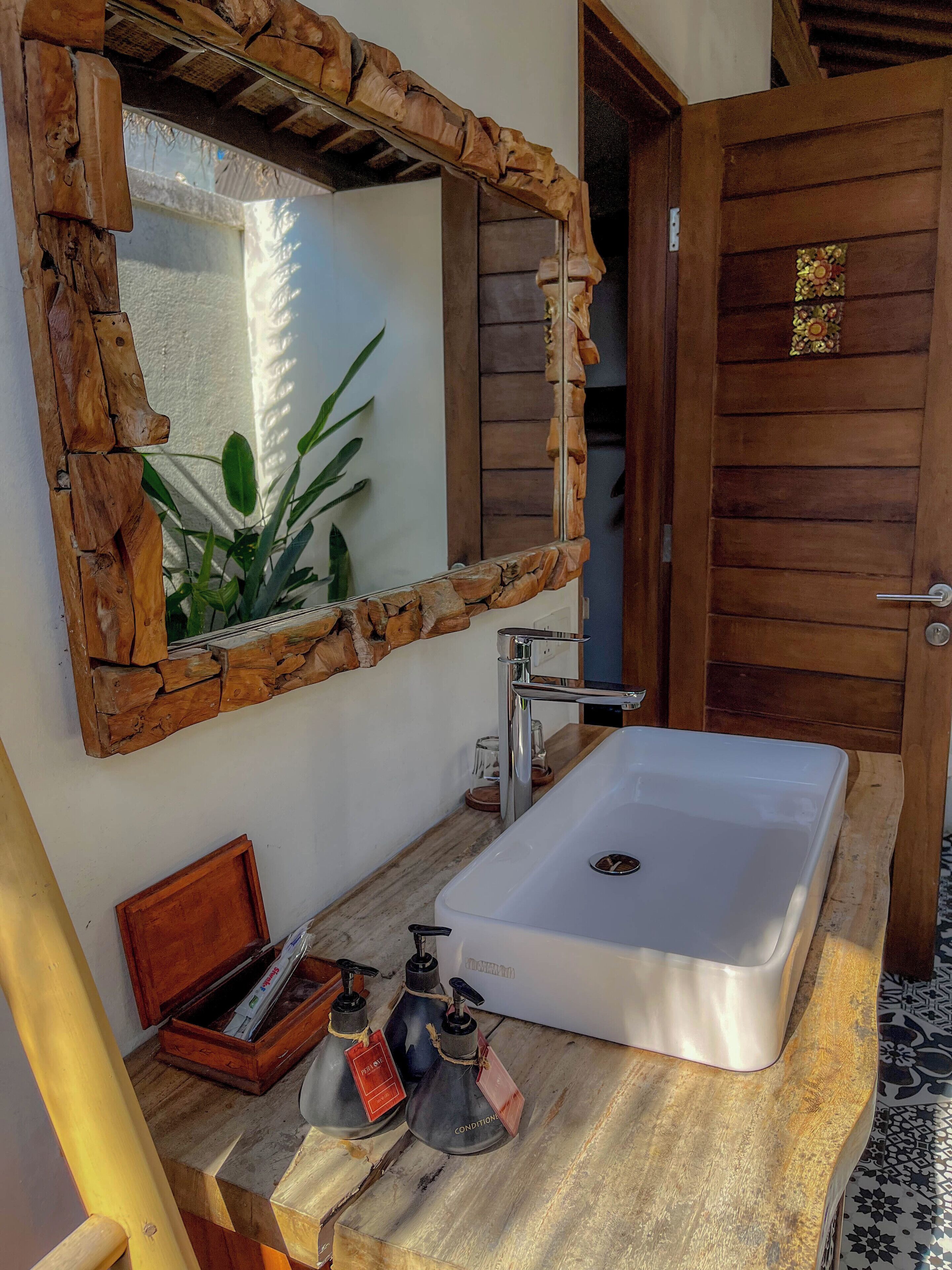 Une salle de bain avec un miroir encadré en bois, un lavabo blanc et un meuble-lavabo en bois.