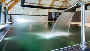 An indoor swimming pool with a clear water surface, a metal handrail, and a wooden ceiling structure. - Hotel Nederheide (Milheeze)