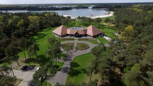 A large building with a central courtyard, surrounded by trees and a lake in the background. - Hotel Nederheide (Milheeze)