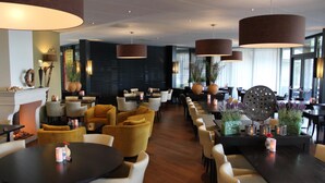 A modern restaurant with round tables, yellow and white chairs, and large hanging lamps. - Hotel Nederheide (Milheeze)