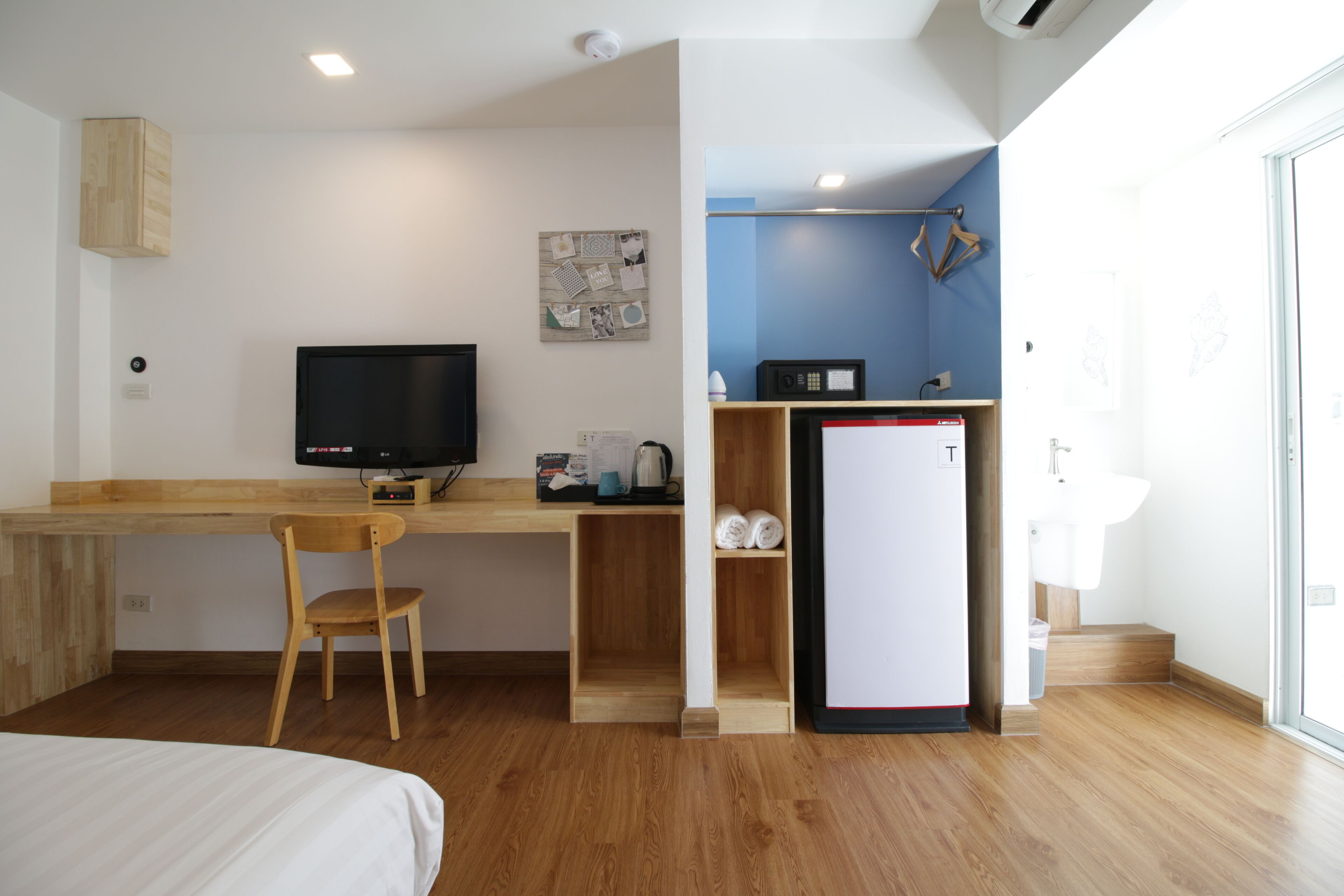 Een kleine hotelkamer met een houten bureau, een televisie, een minibar, een wastafel en een bed.