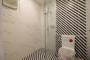 A bathroom with marble tiles, a shower with a glass door, and a toilet with a black and white striped wall.