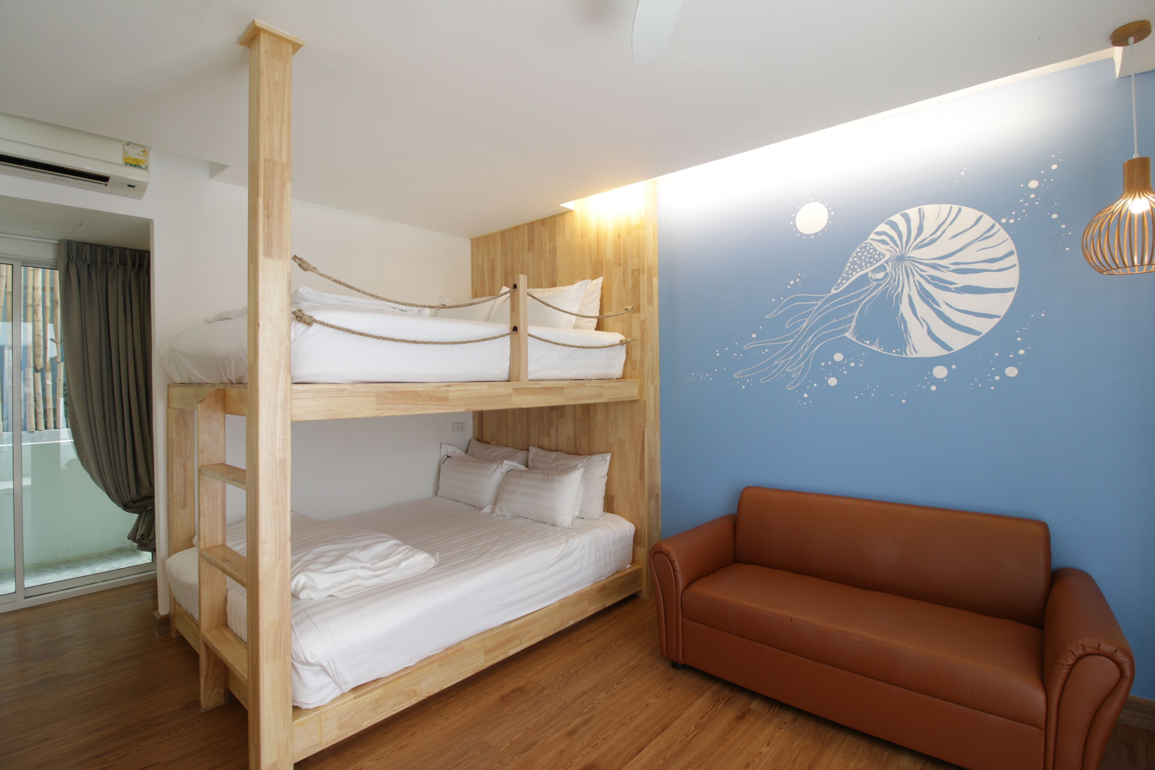 A bunk bed with white bedding, a brown sofa, and a wall with a sea creature mural.