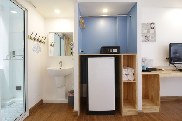 Un baño moderno con cabina de ducha de vidrio, un lavamanos, un espejo, un perchero y un microondas, además de una estantería de madera con toallas.