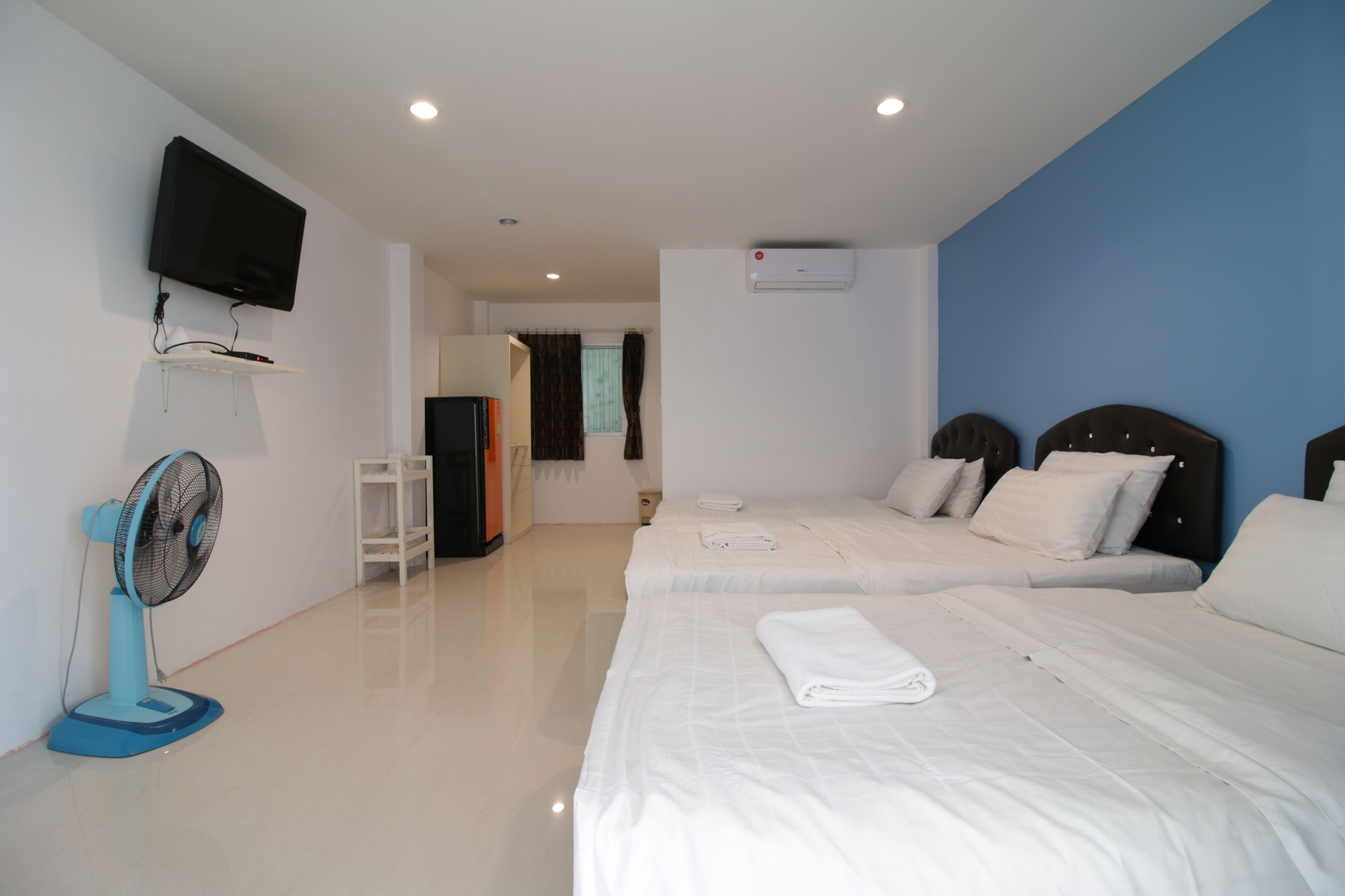 Una habitación de hotel con dos camas, un televisor montado en la pared, un ventilador de pie y un aire acondicionado.
