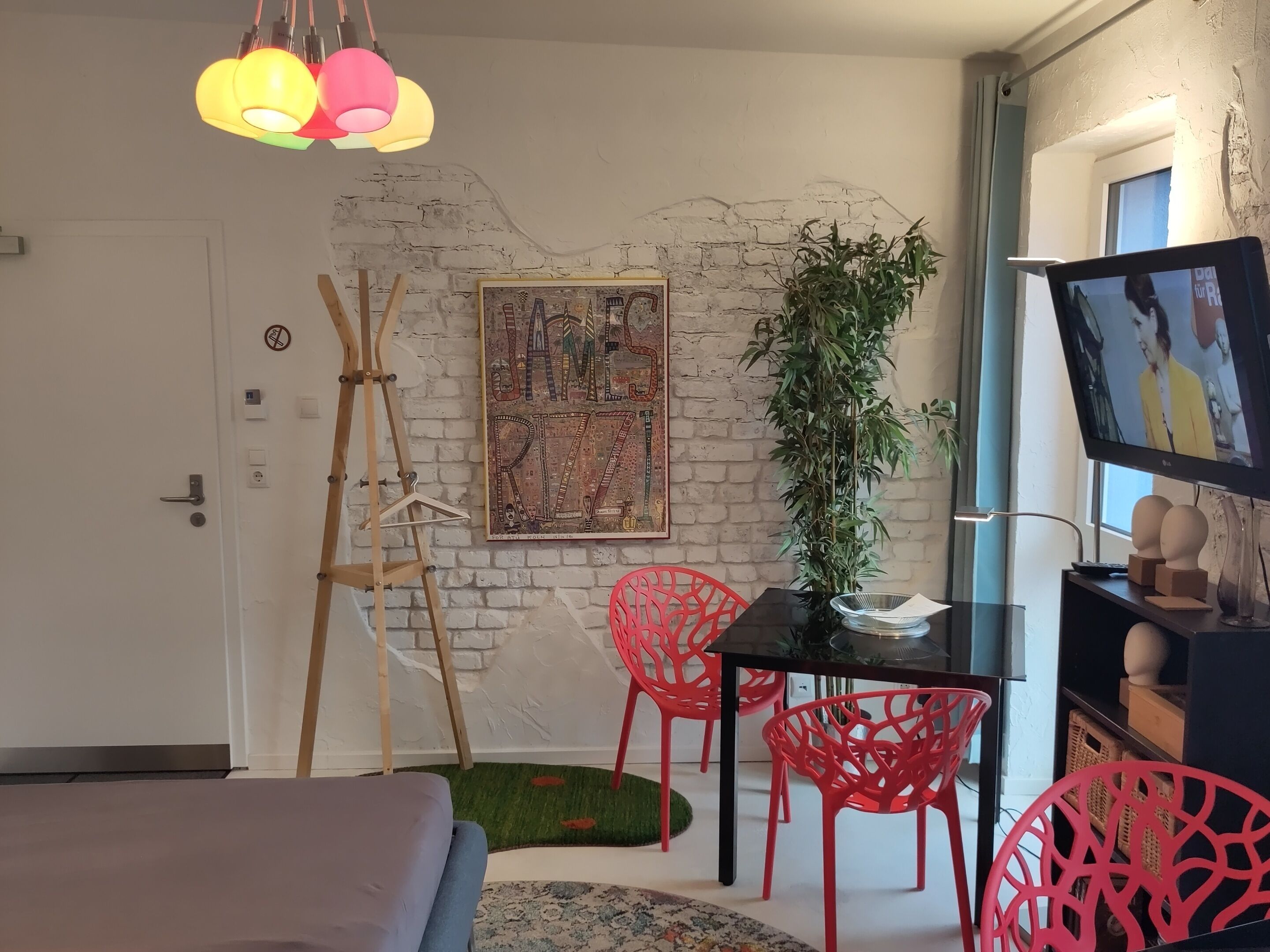 A modern room with a bed, a desk with a chair, a TV, and a plant.