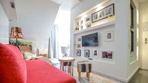 A modern living room with a red sofa, a small round table, and a TV mounted on the wall. - K314 Bonn Aparthotel - Boardinghouse (Bonn)