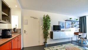 A modern kitchen with a built-in oven, a dining area with a table and chairs, a potted plant, and a television mounted on the wall. - K314 Bonn Aparthotel - Boardinghouse (Bonn)