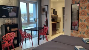 A modern hotel room with a large bed, a desk with a chair, a TV, and a view of the outside. - K314 Bonn Aparthotel - Boardinghouse (Bonn)