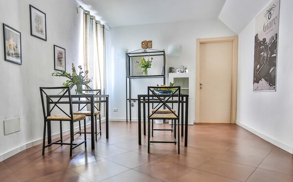 A dining area with two black metal chairs and a table, a shelf with a vase, and framed pictures on the walls. - Le Giare Rooms (Riomaggiore)