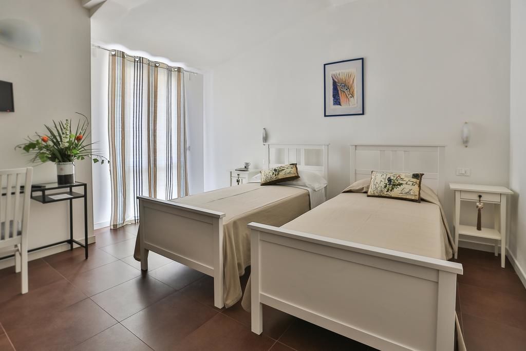 Une chambre avec deux lits simples, une petite table avec une plante, une chaise et une fenêtre avec des rideaux.