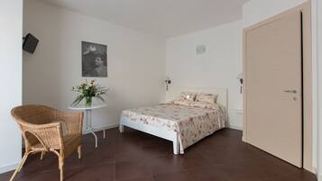 Une chambre à coucher avec un lit, une chaise, une petite table avec une plante et une porte.