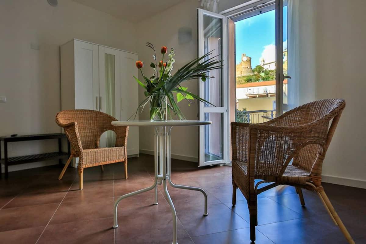 A room with a table and two wicker chairs, a white cabinet, and a view through a glass door.