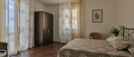 A bedroom with a bed, a wardrobe, a chair, and a window with curtains.