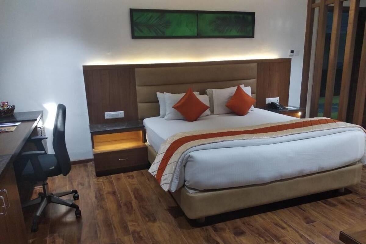 A hotel room with a bed, desk, chair, and a wall-mounted artwork.