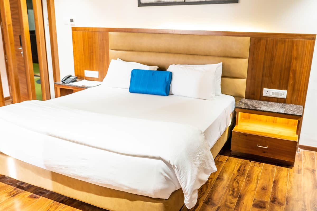 A hotel room with a large bed, wooden headboard, bedside tables, and a nightstand with a phone.