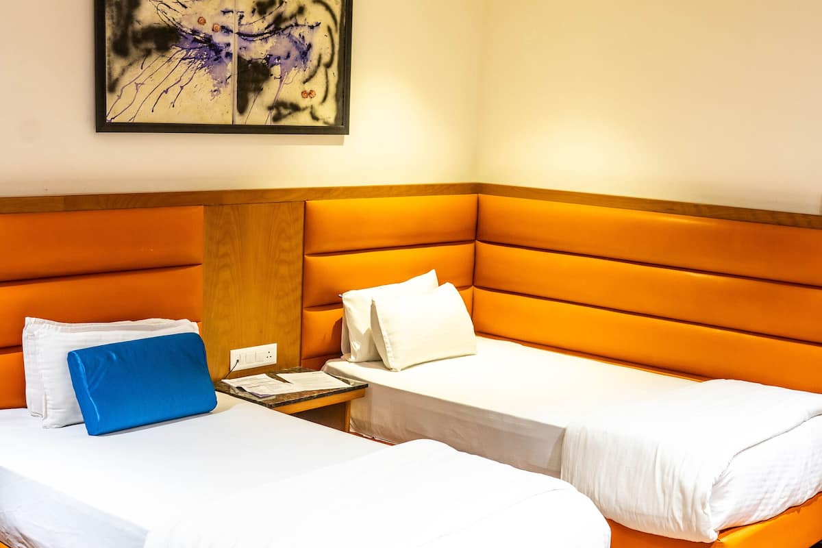 A hotel room with two beds, a wooden floor, a painting on the wall, and a desk with a chair.