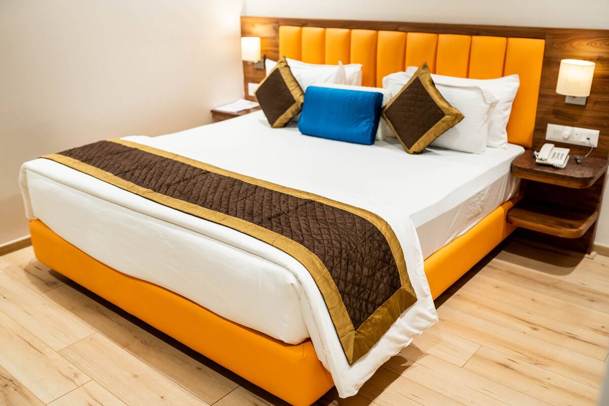 A hotel room with a large bed, wooden headboard, and a nightstand with a phone.