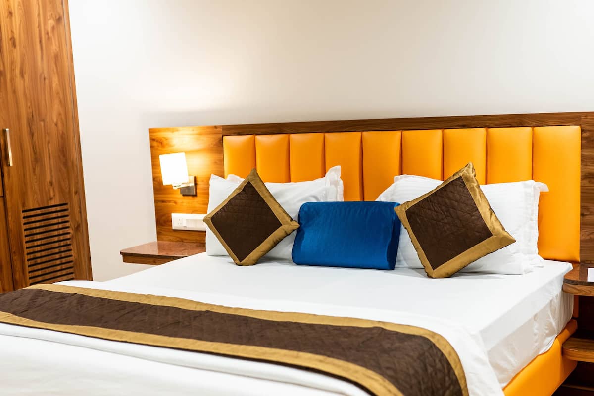 A hotel room with a large bed, wooden wardrobe, and a nightstand with a lamp.