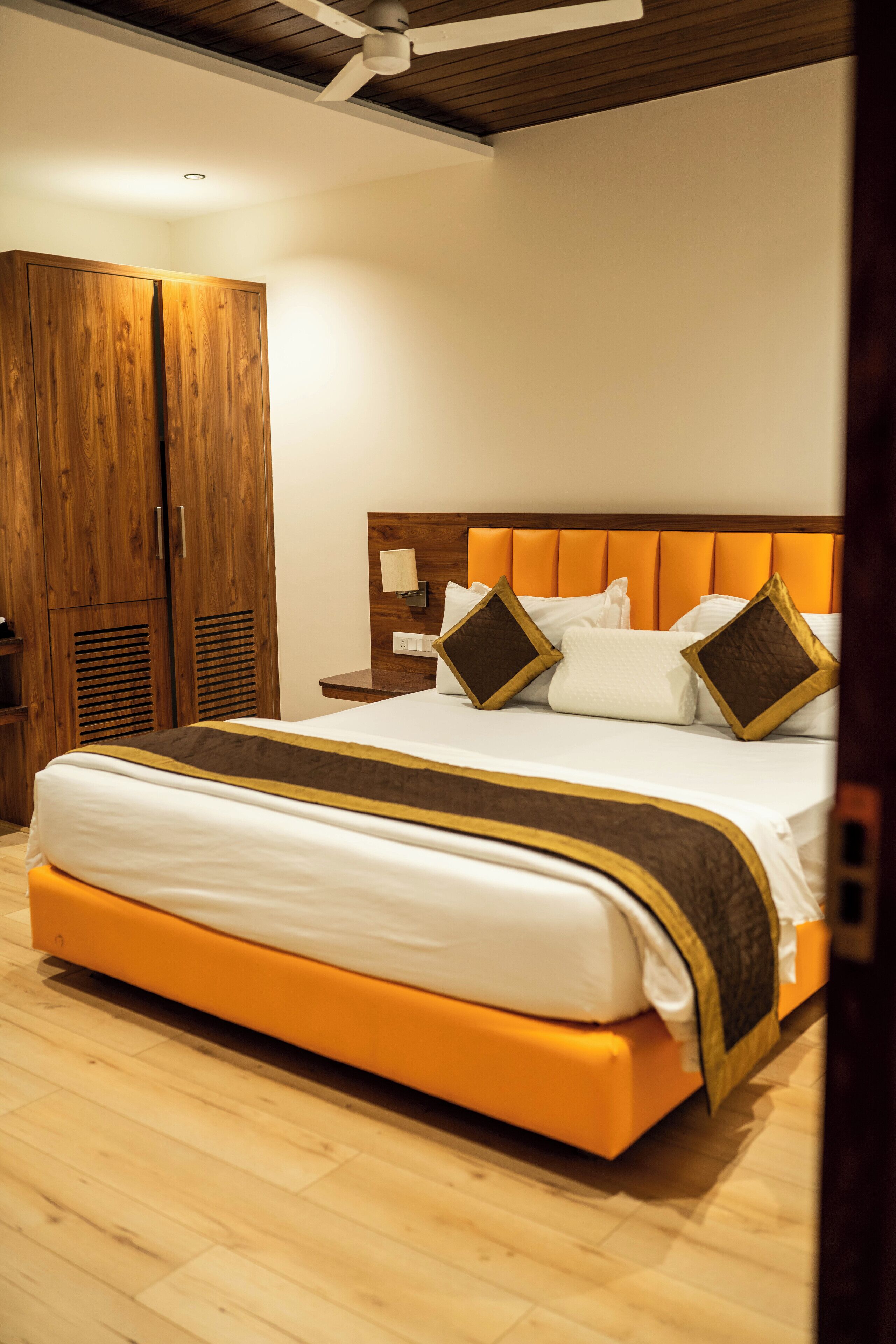 A bedroom with a large bed, wooden wardrobe, and a nightstand with a lamp.