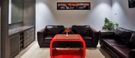 A modern living room with two leather sofas, a red coffee table, and a painting on the wall.