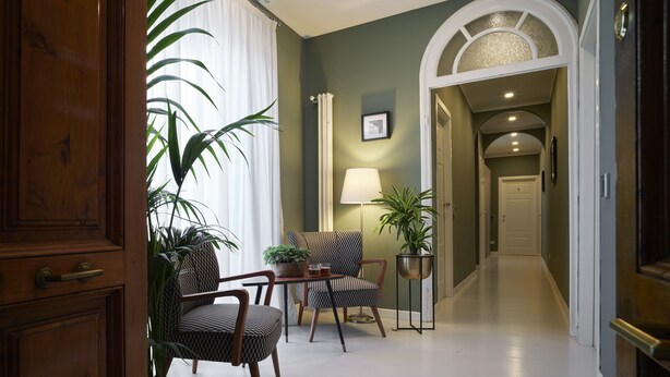 A hallway with a wooden door, a potted plant, two patterned chairs, a table with a lamp, and a framed picture on the wall. - B&B My Way (Florence)