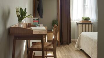 A room with a wooden desk, a chair, a bed, a television mounted on the wall, and a window with curtains.