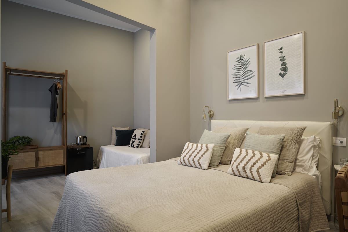 Une chambre à coucher comprenant un grand lit, une table de chevet, une commode, une armoire et deux reproductions botaniques encadrées accrochées au mur.