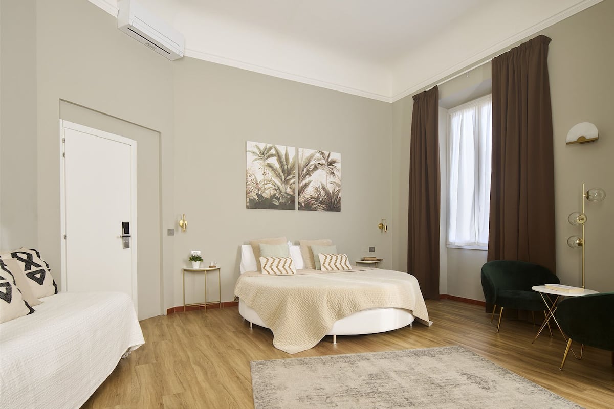 Une chambre à coucher comprenant un lit, des tables de chevet, une chaise, une fenêtre avec des rideaux et un climatiseur fixé au mur.