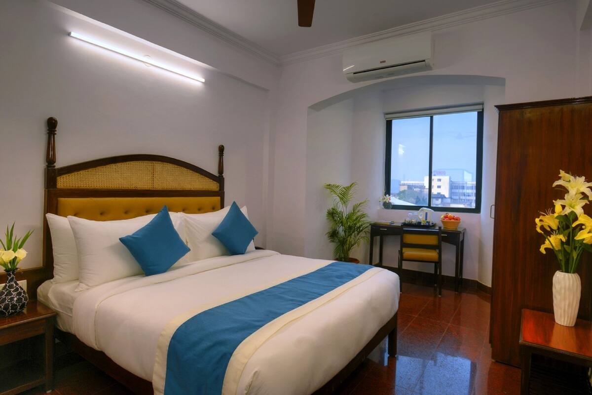 A hotel room with a large bed, a desk, a chair, and a view of the city through the window.