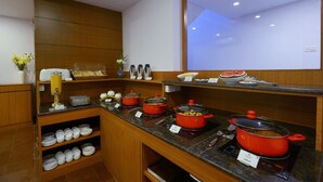 A buffet area with multiple food stations, including a hot pot and various dishes. - TreeHouse Neptune Inn (Panaji)
