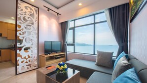 A modern living room with a sofa, a coffee table, a TV, and a view of the sea. - Handy Beachfront Apartment (Bac Nha Trang)