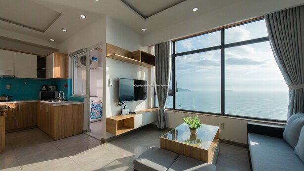 A modern living room with a sofa, a coffee table, a TV, and a large window with a view of the sea. - Handy Beachfront Apartment (Bac Nha Trang)
