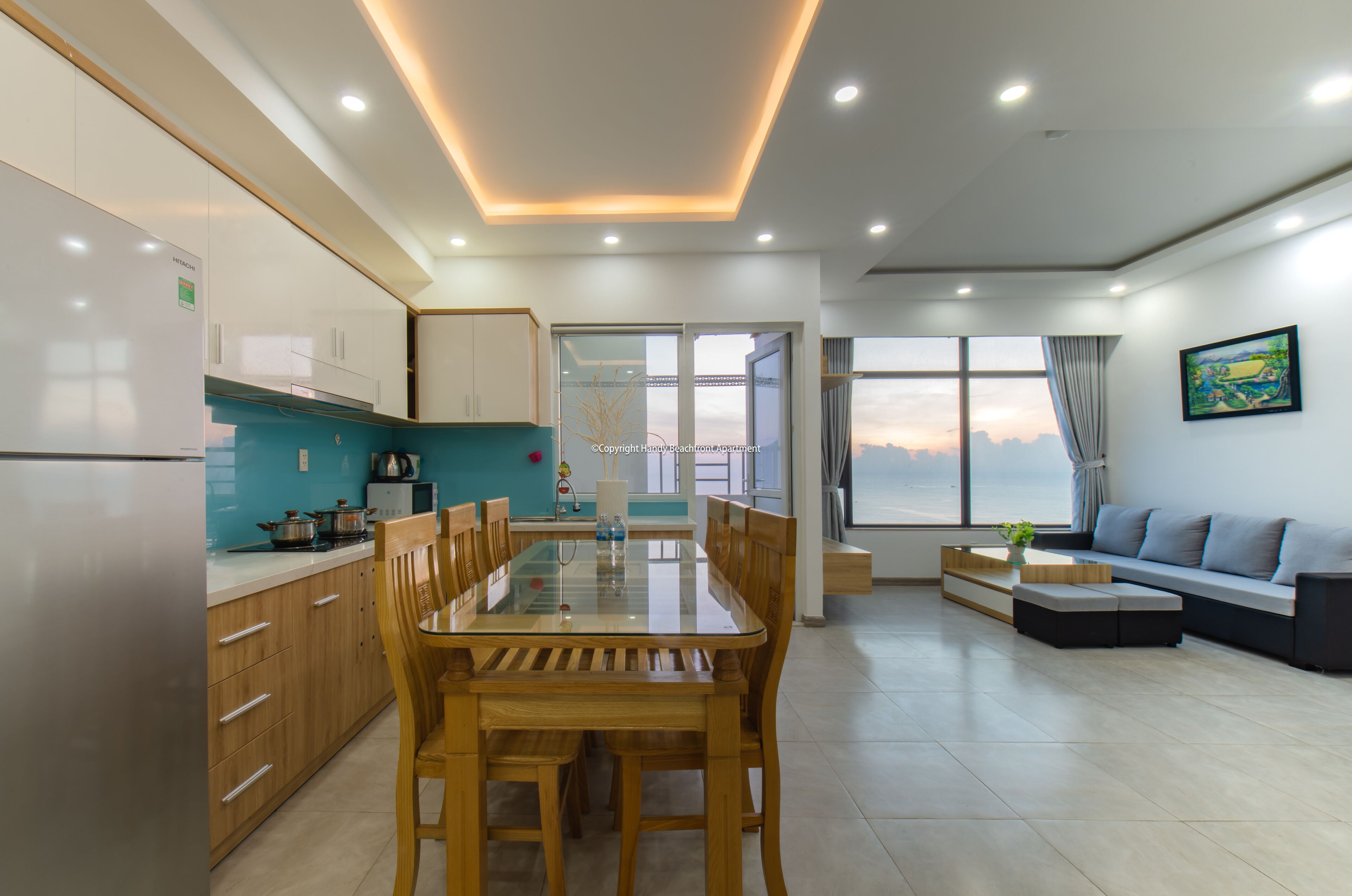 A modern kitchen with wooden cabinets, a glass dining table, and a view of a bridge through the glass door.