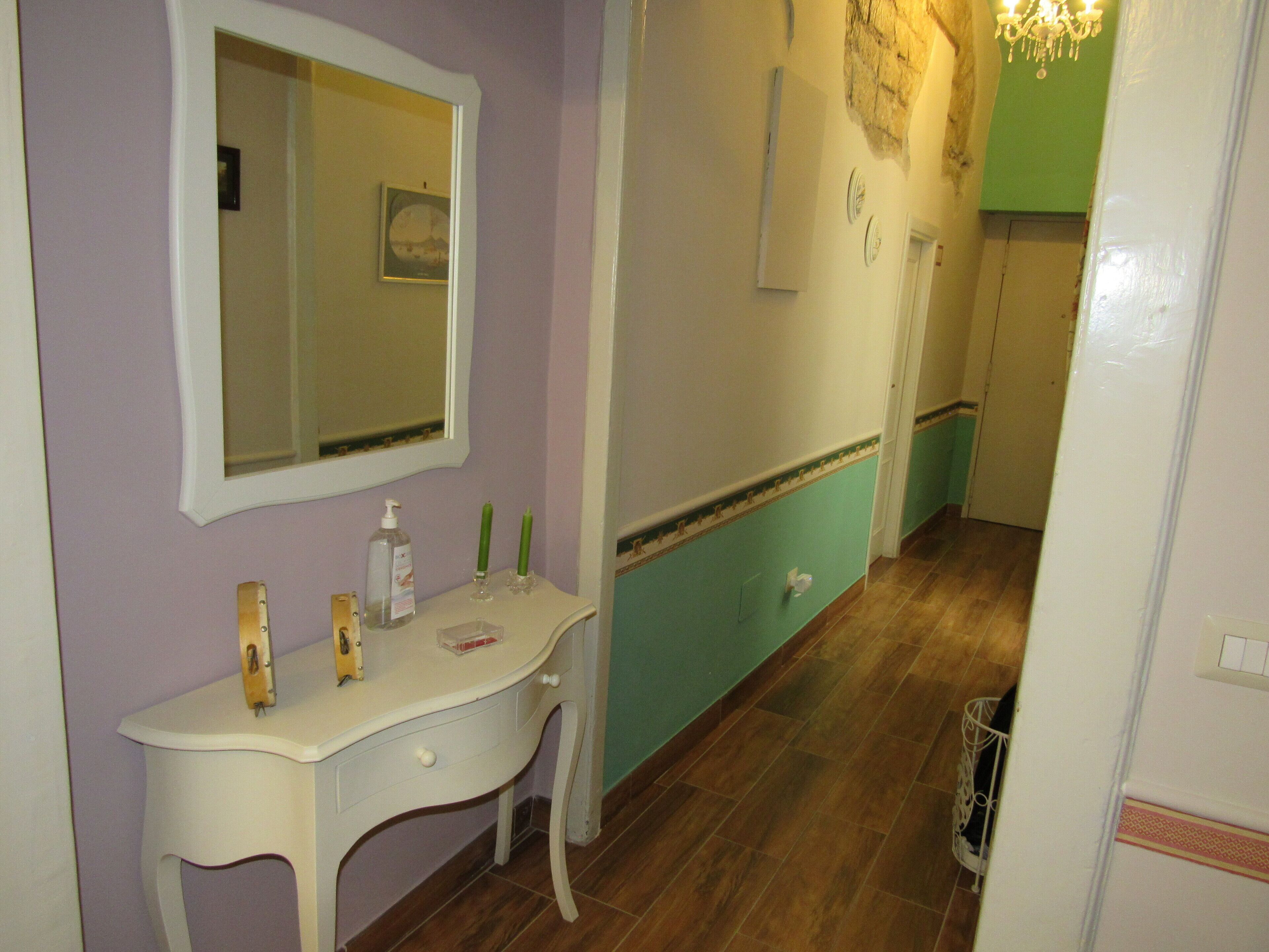 Un bagno con un mobile lavabo bianco, uno specchio, una parete verde, un pavimento in legno e un lampadario.