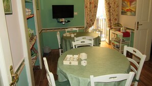 A dining area with a green table, white chairs, a television on the wall, and a painting on the wall. - B&B Speranzella (Naples)