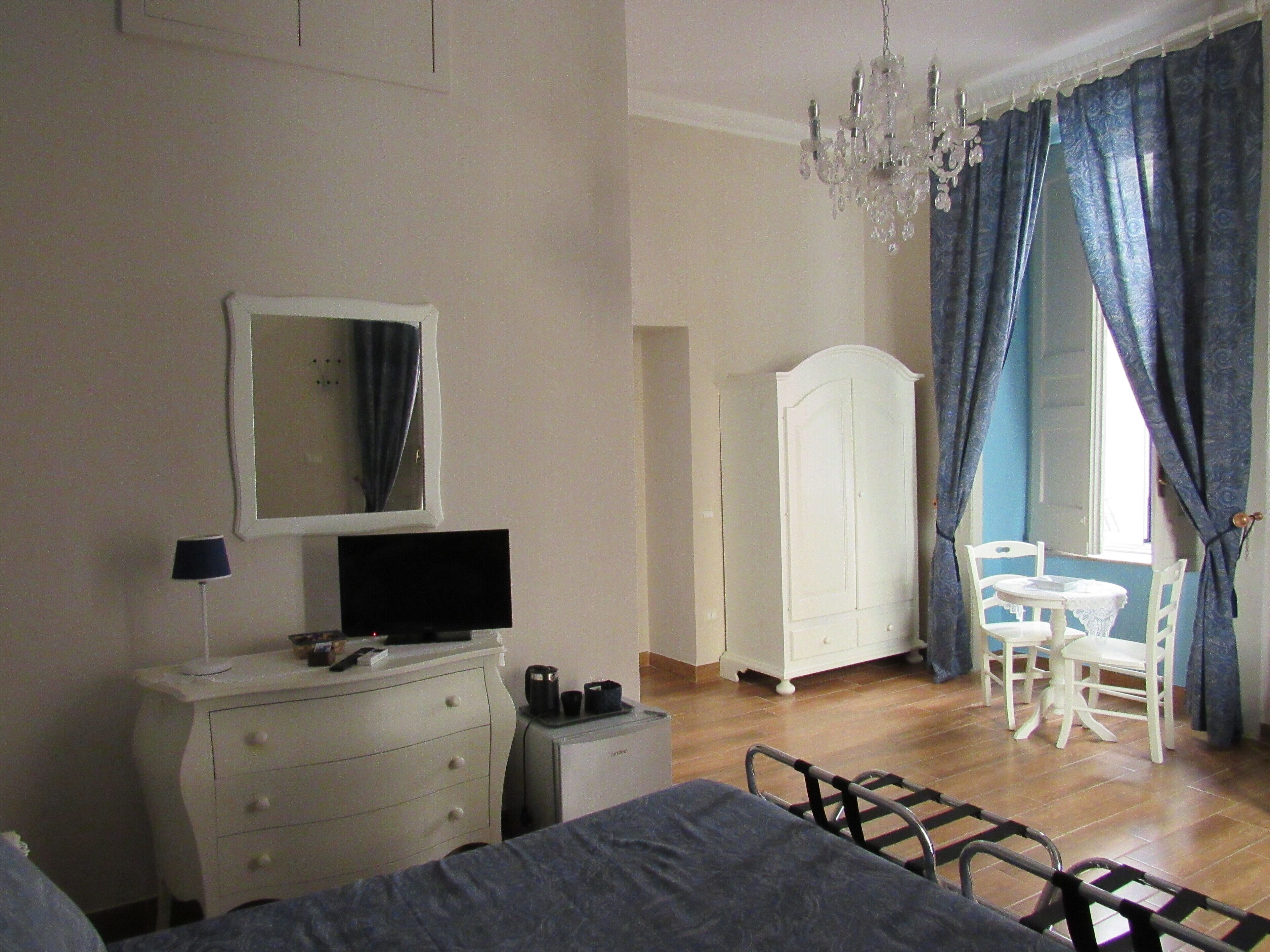 A bedroom with a bed, dresser, TV, wardrobe, and a dining area with chairs and a table.