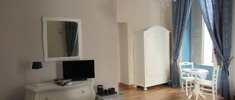 A bedroom with a bed, dresser, TV, wardrobe, and a dining area with chairs and a table.