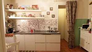 A compact kitchen with a tiled backsplash, a gas stove, a sink, and a microwave. There are shelves above the counter holding various kitchen items. - B&B Speranzella (Naples)