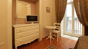 A bedroom with a dresser, a television, a chair, and a window with curtains. - B&B Speranzella (Naples)