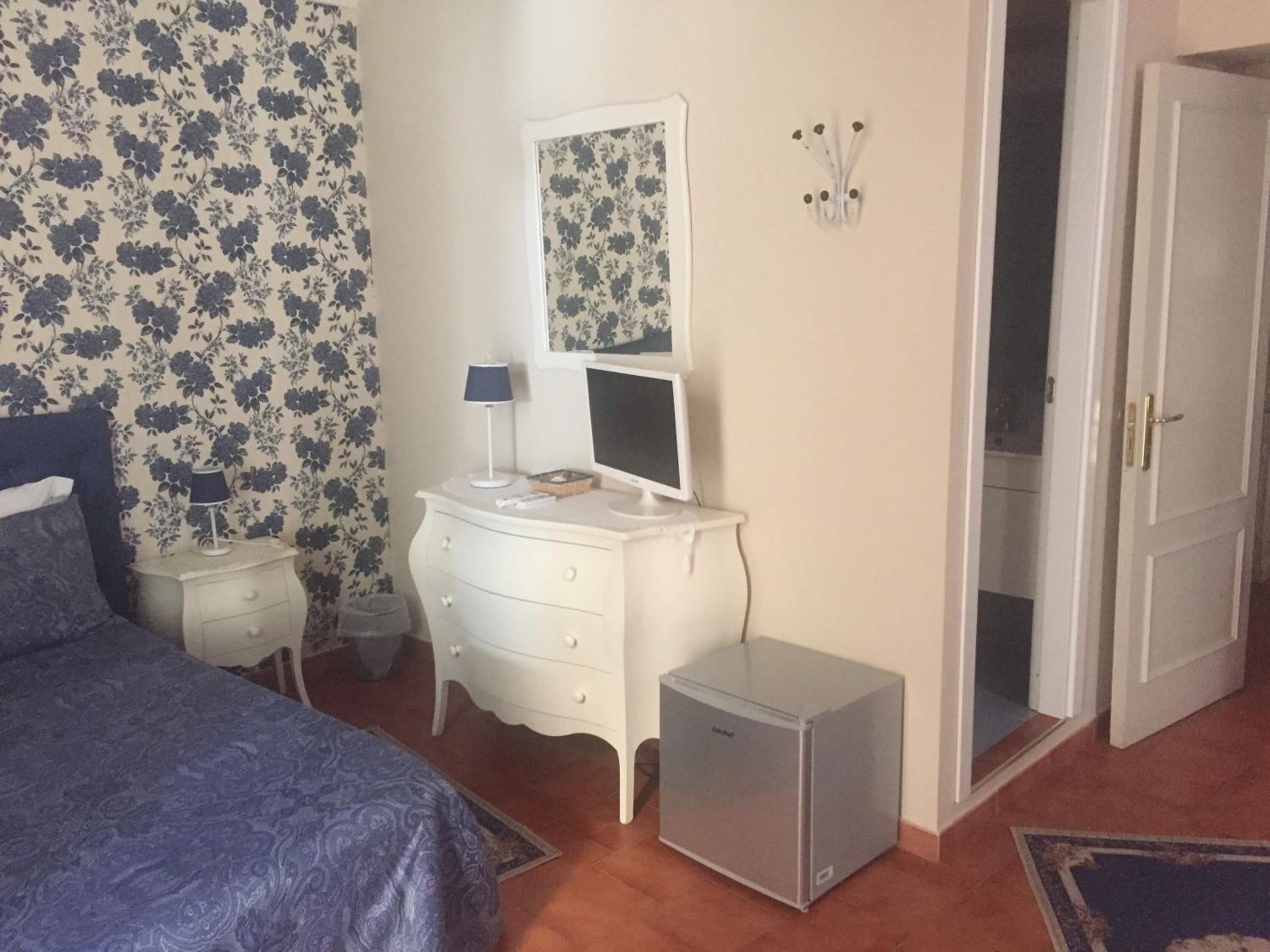 Une chambre à coucher comprenant un lit, une commode, un petit réfrigérateur, une table de chevet avec une lampe et un tableau accroché au mur.