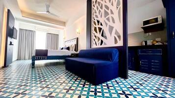 Una habitación de hotel con cama, sofá, separador decorativo, kitchenette y suelo estampado.