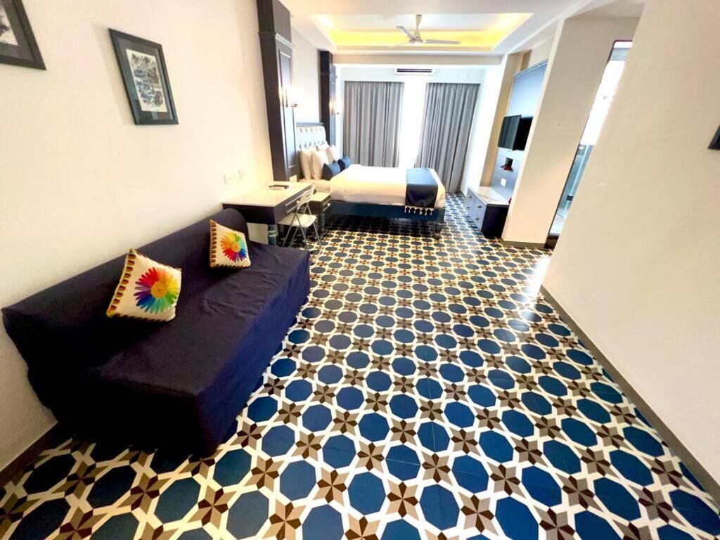 Habitación de hotel con una cama grande, un escritorio y una silla. El suelo presenta un diseño y hay un ventilador de techo.